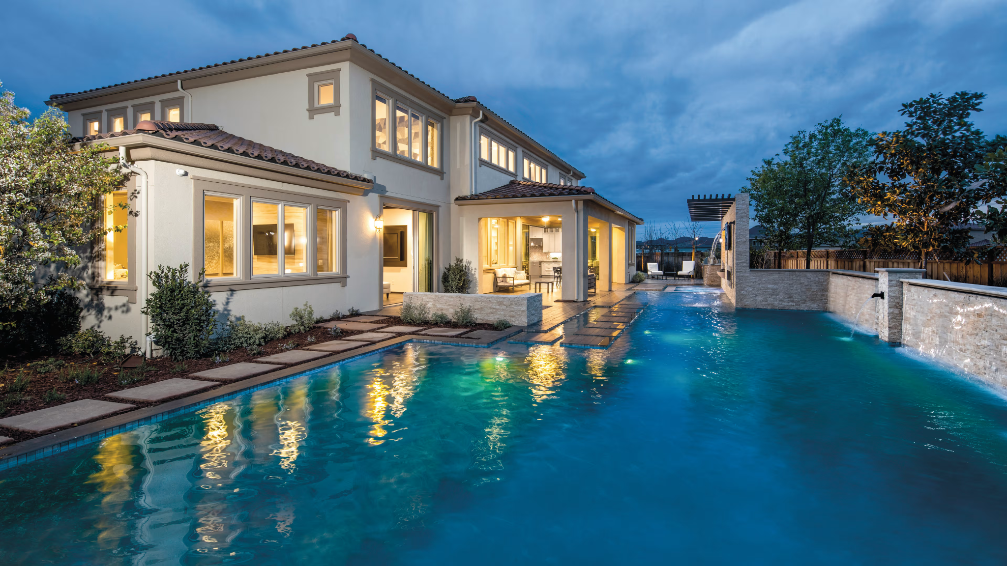 An illuminated backyard swimming pool beside a contemporary home at dusk